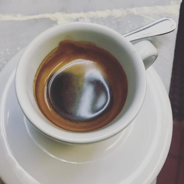 Close-up of a rich, dark espresso in a white cup and saucer with a spoon.