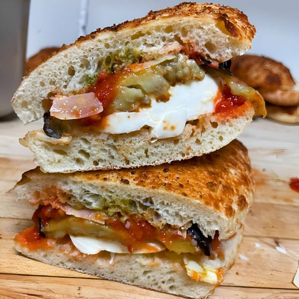 A Clemente's Pizzeria & Cafe Italiano sandwich, cut in half, revealing fresh mozzarella, tomato sauce, and vegetables.