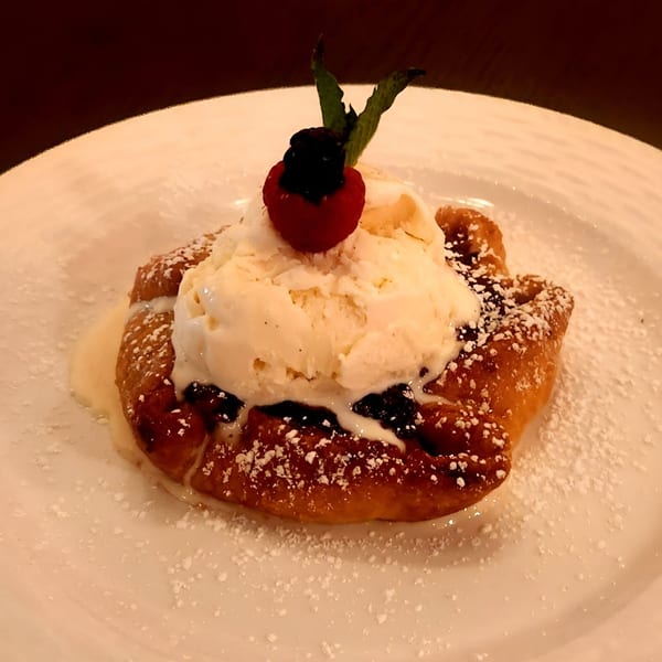 Warm Italian pastry topped with vanilla ice cream, raspberry, blackberry, and mint on a white plate.