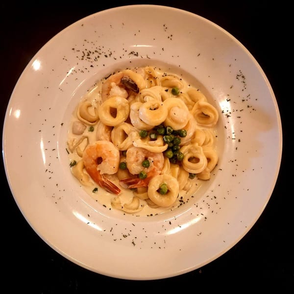 Creamy tortellini pasta with shrimp and green peas, garnished with herbs on a white plate.