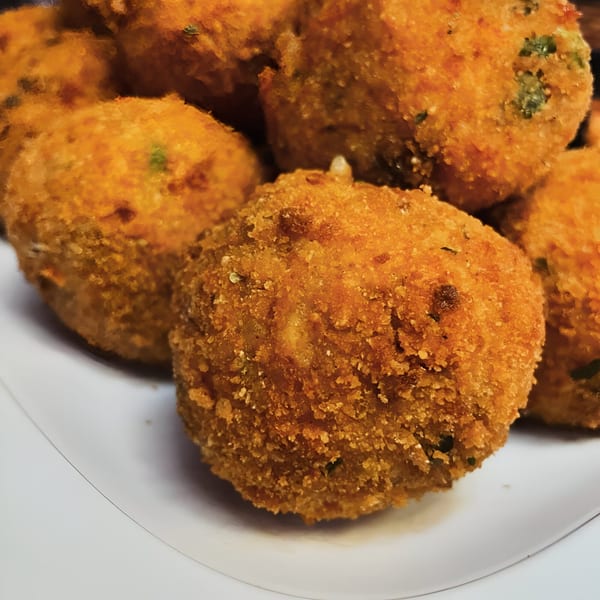 Close-up of golden-brown, breaded arancini balls on a white plate, showcasing their crispy texture.