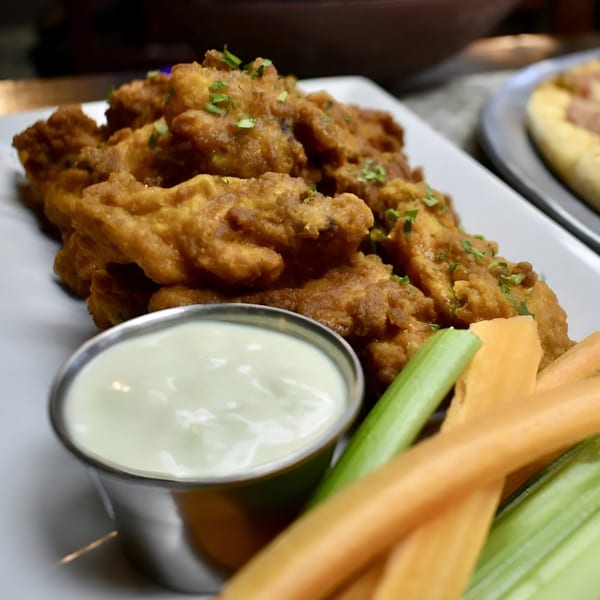 Crispy fried chicken wings with ranch dressing, celery, and carrot sticks on a white plate.