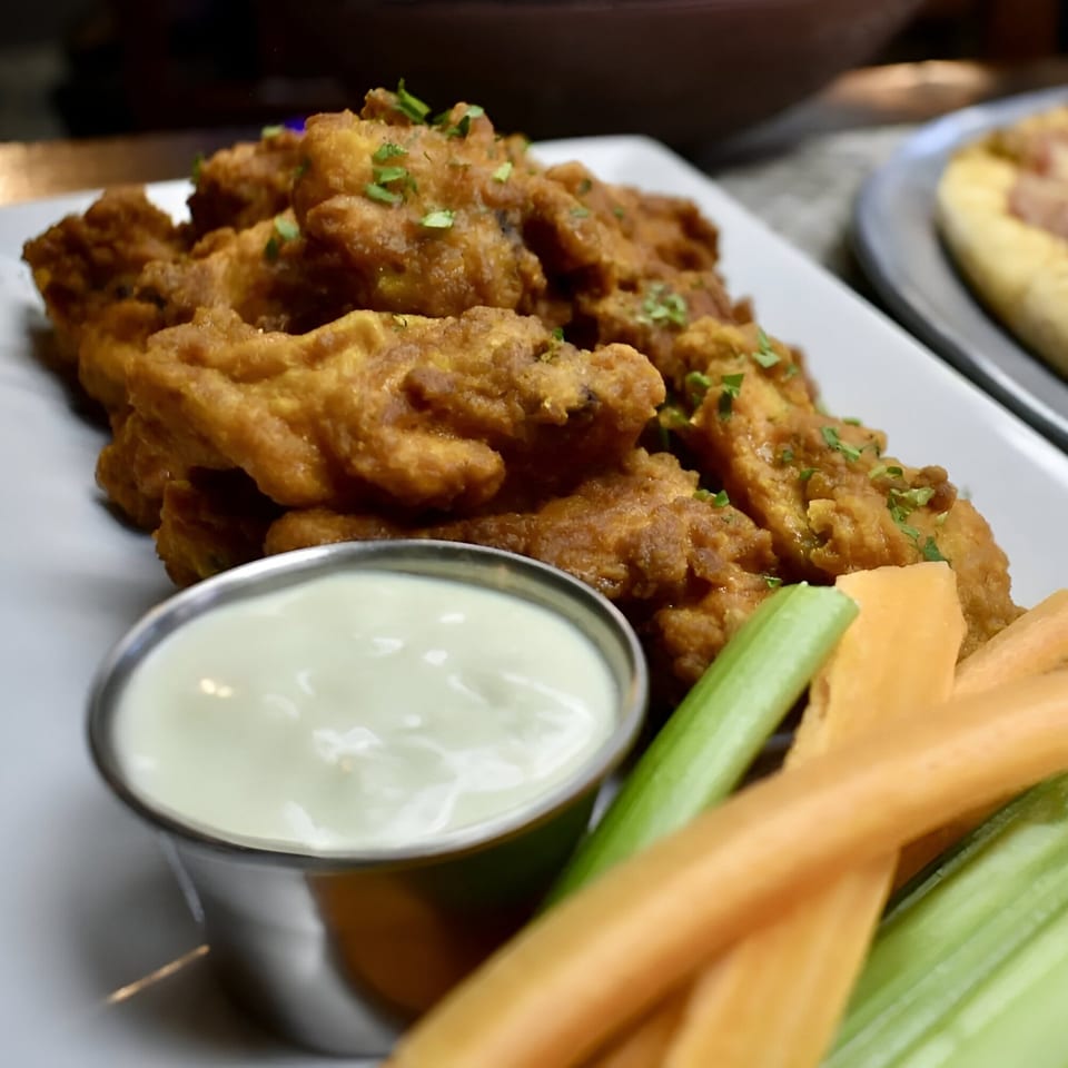 Crispy fried chicken wings with ranch dressing, celery, and carrot sticks on a white plate.