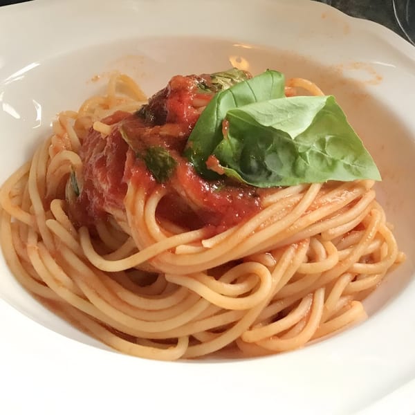 Spaghetti with red tomato sauce and fresh basil leaves in a white bowl at Clemente's Pizzeria.