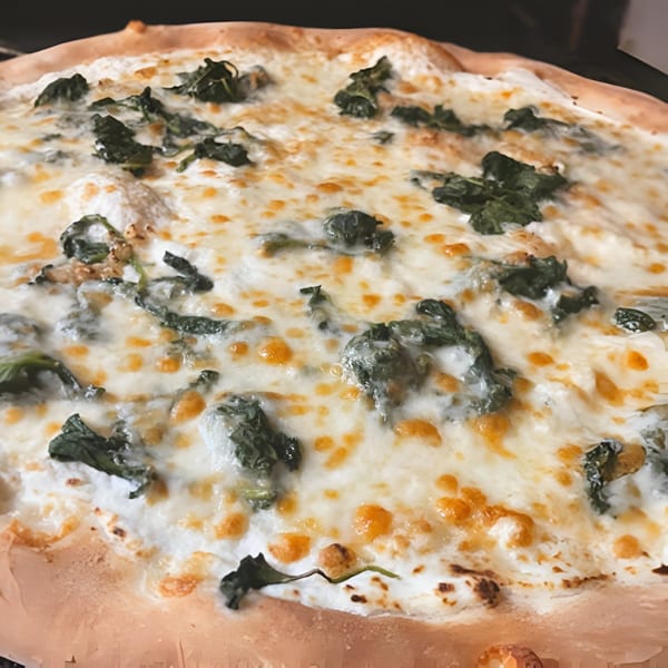 Close-up of a Clemente's Pizzeria & Cafe Italiano white pizza with spinach and melted cheese.
